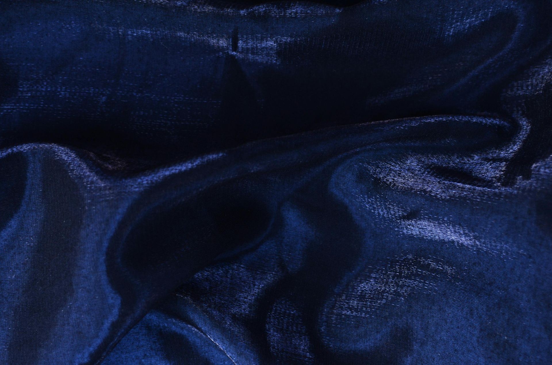 Close-up of smooth, shiny dark blue fabric with soft folds and reflective surface.